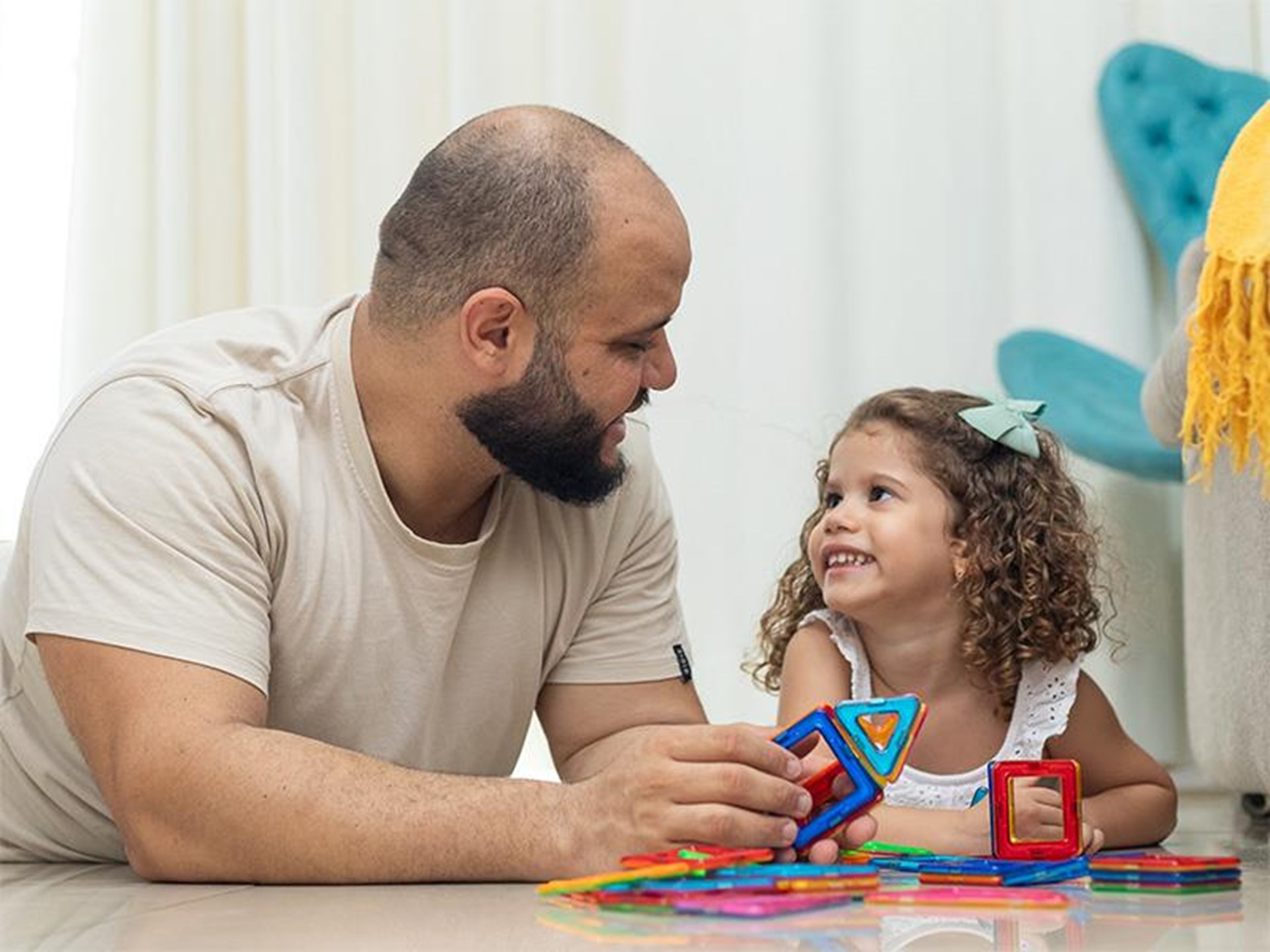 Bärtiger Mann und kleines Mädchen mit Locken spielen auf dem Boden mit bunten Bauklötzen