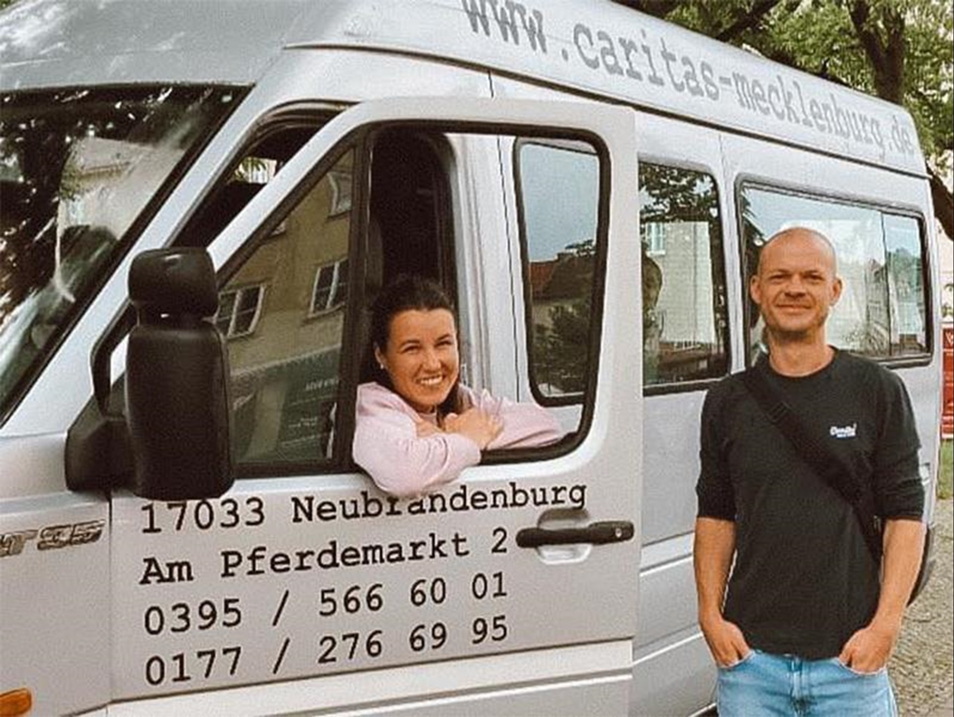 eine Frau und ein Mann stehen vor einem grauen Transporter