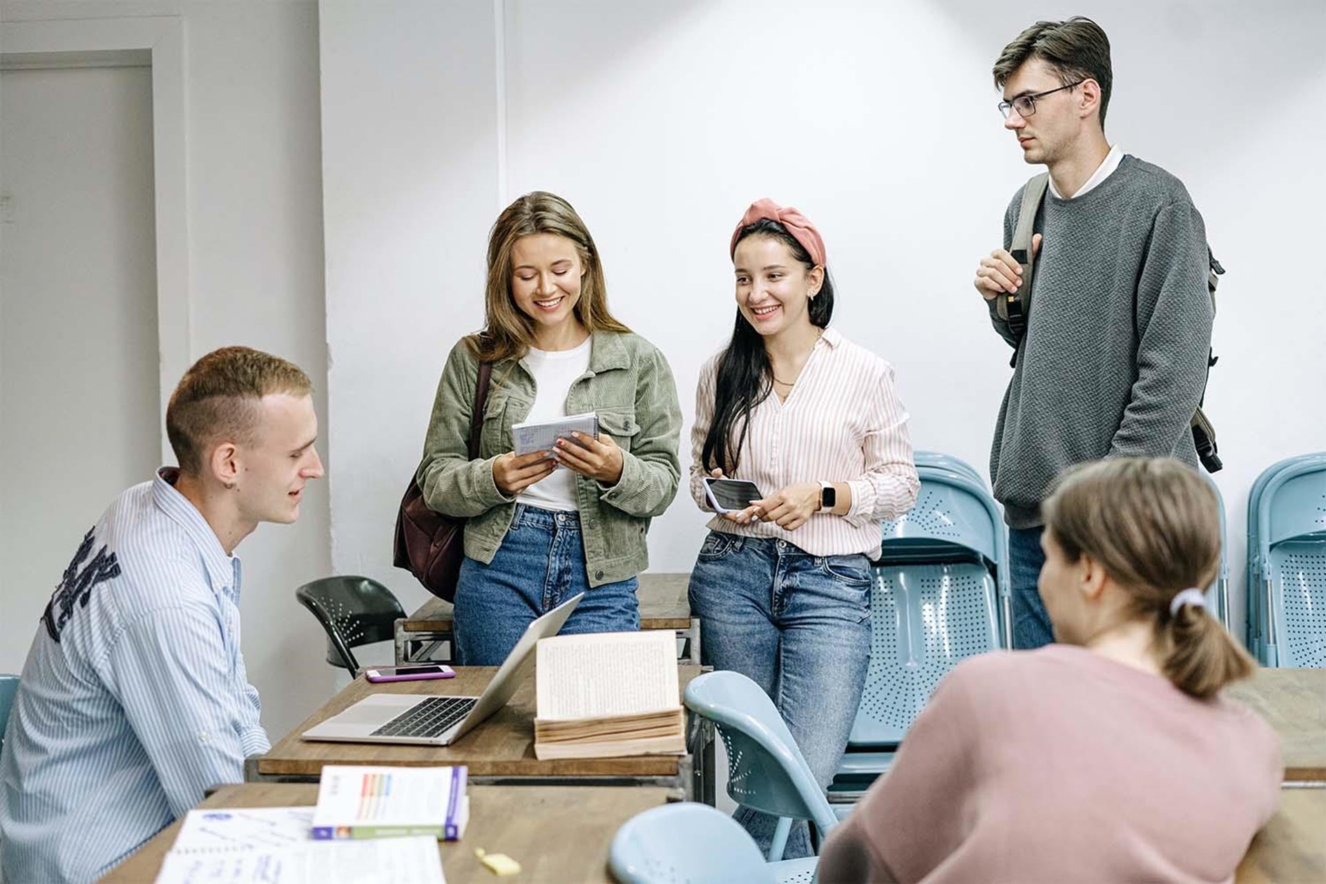 Fünf Jugendliche stehen und sitzen in einem Klassenraum.