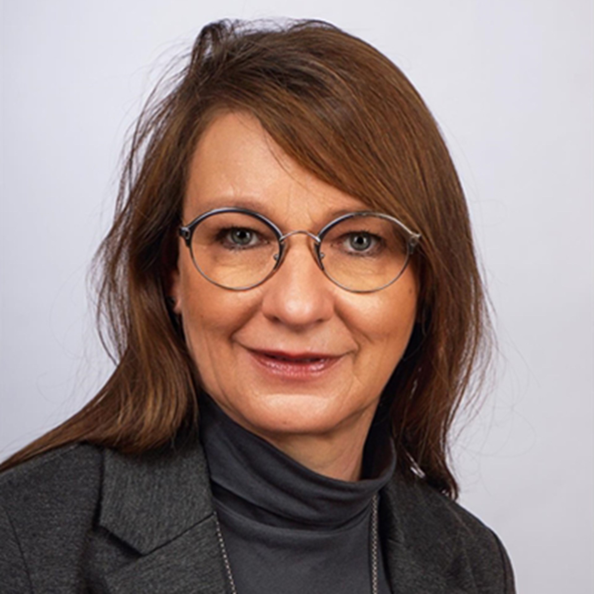 Lächelnde Frau mit langen, braunen Haaren und Brille, die schwarze Oberbekleidung trägt