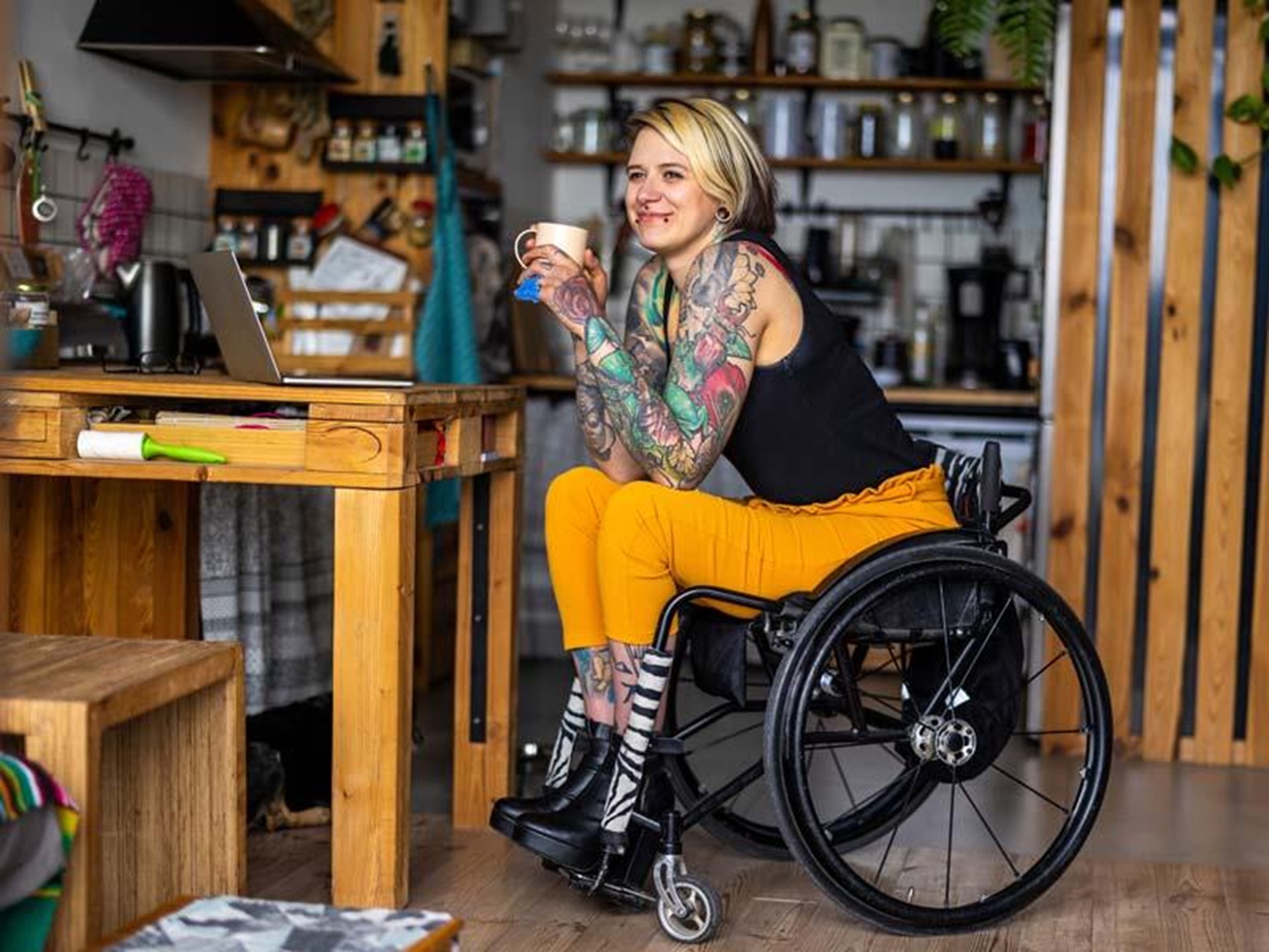 Zufriedene junge Frau mit Tattoos im Rollstuhl in häuslicher Umgebung 
