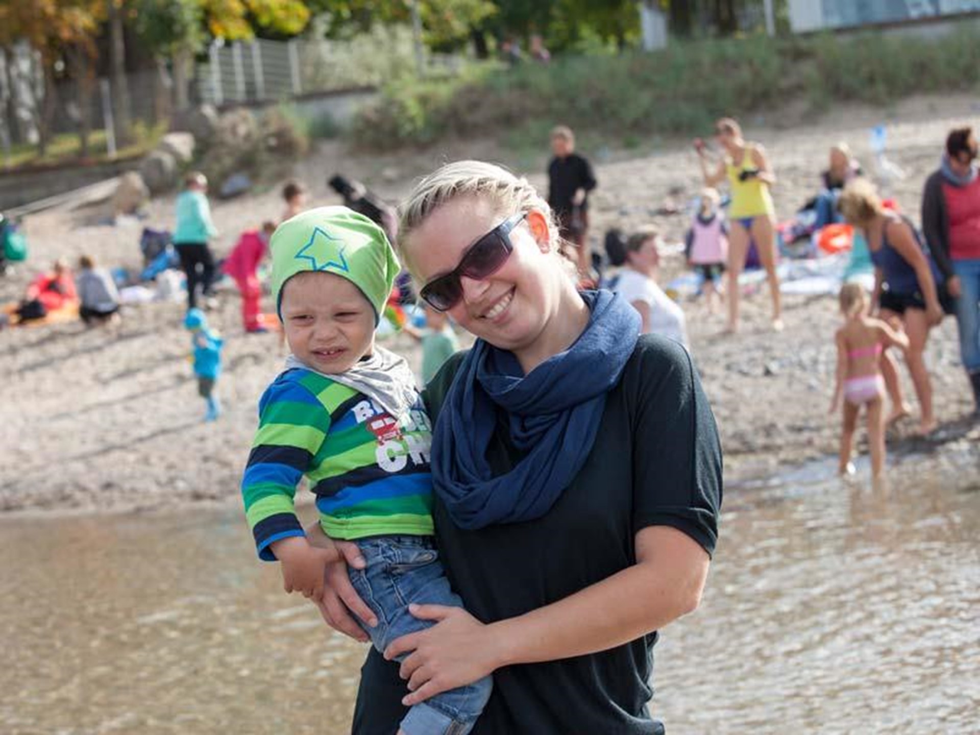 Mutter mit kleinem Kind auf dem Arm am belebten Ostseestrand